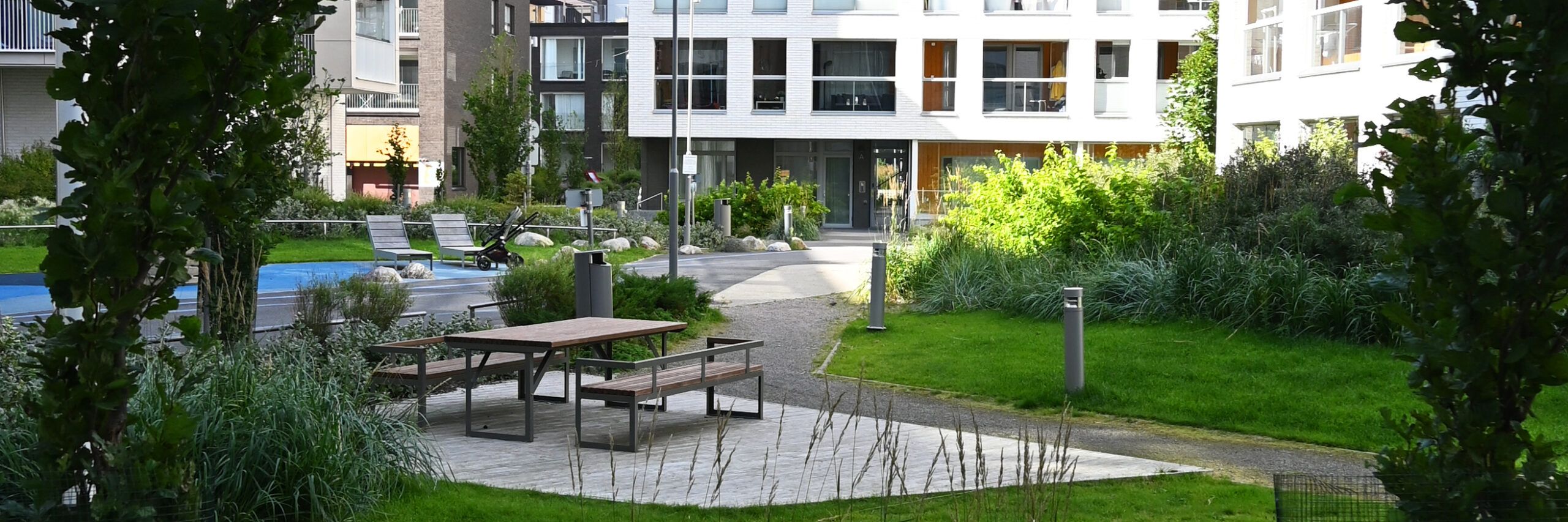 Kuvassa on kerrostalon piha, jossa on useita oleskeluryhmiä ja paljon kasvillisuutta.